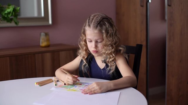 Adorable happy little girl drawing with pencils at the home at the white table in cozy childs room. Concept of child creative activity. Shooting in slow motion.