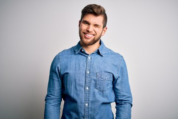 Young handsome blond man with beard and blue eyes wearing casual denim shirt winking looking at the...