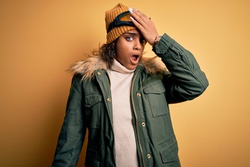 Young african american afro skier girl wearing snow sportswear and ski goggles surprised with hand on head for mistake, remember error. Forgot, bad memory concept.