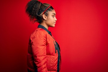 Beautiful african american girl wearing red jacket and sunglasses over isolated background looking to side, relax profile pose with natural face with confident smile.