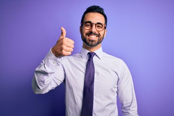 Handsome businessman with beard wearing casual tie and glasses over purple background doing happy thumbs up gesture with hand. Approving expression looking at the camera showing success.