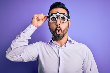 Obraz premium Young handsome optical man with beard wearing optometry glasses over purple background scared in shock with a surprise face, afraid and excited with fear expression