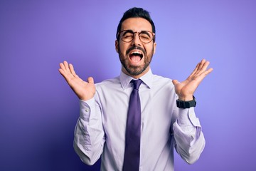 Handsome businessman with beard wearing casual tie and glasses over purple background celebrating mad and crazy for success with arms raised and closed eyes screaming excited. Winner concept