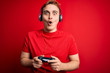 Young handsome redhead gamer man playing video game using headphones and joystick scared and amazed with open mouth for surprise, disbelief face © Krakenimages.com
