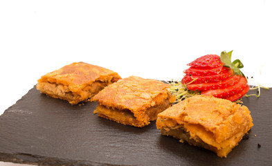 Pieces of Galician pie on slate plate decorated with strawberries on white background
