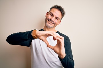 Young handsome man wearing casual t-shirt standing over isolated white background smiling in love doing heart symbol shape with hands. Romantic concept.