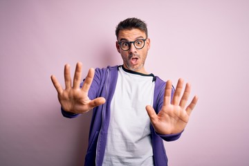 Naklejka premium Young handsome man wearing purple sweatshirt and glasses standing over pink background doing stop gesture with hands palms, angry and frustration expression