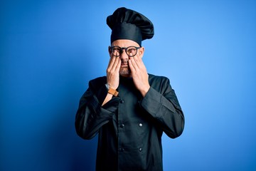 Young handsome chef man wearing cooker uniform and hat over isolated blue background rubbing eyes for fatigue and headache, sleepy and tired expression. Vision problem