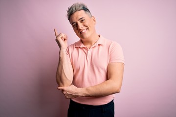 Young handsome modern man wearing casual pink t-shirt over isolated background with a big smile on face, pointing with hand and finger to the side looking at the camera.