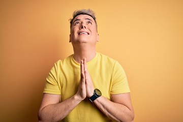 Young handsome modern man wearing yellow shirt over yellow isolated background begging and praying...