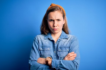 Young beautiful blonde woman wearing casual denim shirt and diadem over blue background skeptic and...