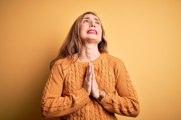 Young beautiful blonde woman wearing casual sweater standing over yellow background begging and...
