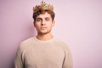 Young blond man with curly hair wearing golden crown of king over pink background Relaxed with...
