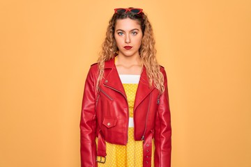 Young beautiful blonde woman pin-up with blue eyes wearing red sunglasses and jacket with serious expression on face. Simple and natural looking at the camera.