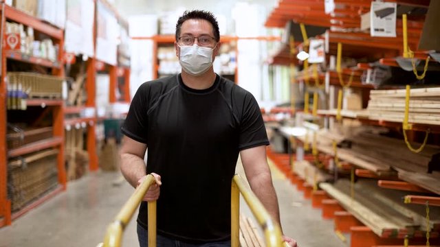 Portrait of Man with face mask shopping for lumber wood in hardware store during global pandemic for home project with PPE on