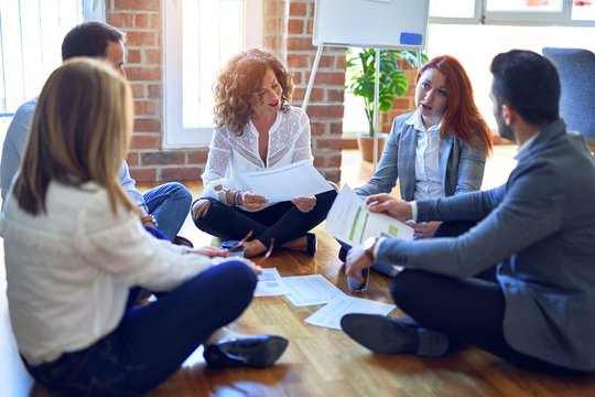Group of business workers smiling happy and confident. Sitting on the floor relaxed working together speaking and reading documents at the office