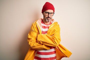Middle age hoary man wearing glasses and rain coat standing over isolated white background skeptic and nervous, disapproving expression on face with crossed arms. Negative person.