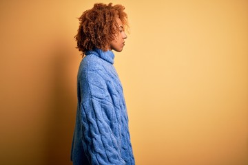 Young beautiful African American afro woman with curly hair wearing blue turtleneck sweater looking to side, relax profile pose with natural face with confident smile.