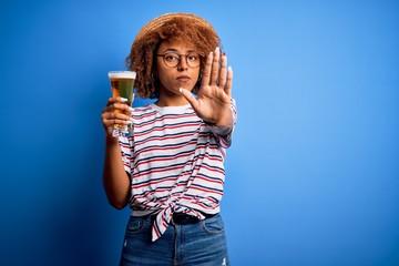 Young beautiful African American afro woman with curly hair on vacation drinking glass of beer with...