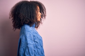 Young beautiful african american woman with afro hair wearing winter sweater over pink background looking to side, relax profile pose with natural face with confident smile.