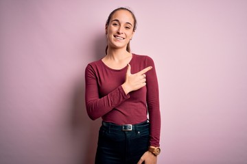 Young beautiful woman wearing casual t-shirt standing over isolated pink background cheerful with a smile of face pointing with hand and finger up to the side with happy and natural expression on face