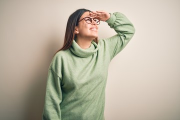 Young beautiful woman wearing casual sweater standing over isolated white background very happy and smiling looking far away with hand over head. Searching concept.