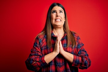 Young beautiful woman wearing casual shirt over red background begging and praying with hands together with hope expression on face very emotional and worried. Begging.