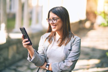 Young beautiful woman smiling happy and confident. Standing with smile on face using smartphone at the city