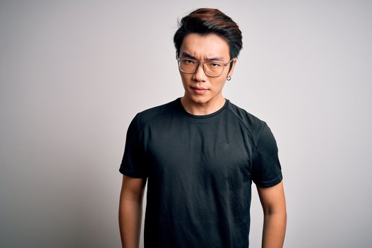 Young handsome chinese man wearing black t-shirt and glasses over white background skeptic and nervous, frowning upset because of problem. Negative person.