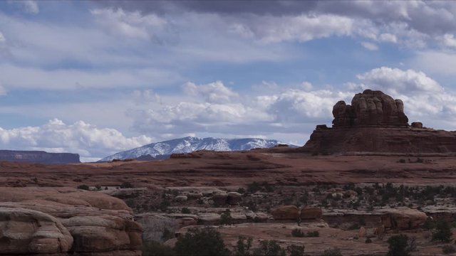 A long-lens timelapse looking across past some red rocks towards the Abajo Mountains close to Monticello. Clouds flow overhead at speed.