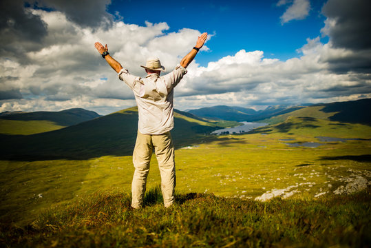 Victorious hiker atop Scottish hill overlooking lake - shallow depth of field