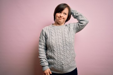 Young down syndrome woman wearing casual sweater over isolated background confuse and wonder about question. Uncertain with doubt, thinking with hand on head. Pensive concept.