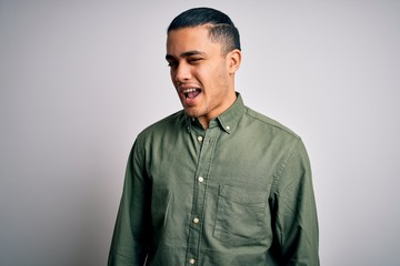 Fototapeta premium Young brazilian man wearing casual shirt standing over isolated white background winking looking at the camera with sexy expression, cheerful and happy face.