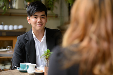 Happy young Asian business couple talking together at the coffee shop