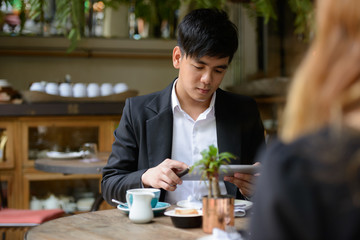 Young Asian business couple together at the coffee shop with man using digital tablet
