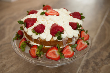 Two layer cake with strawberries and whipped cream on a glass cake platter