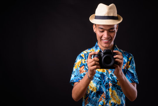 Portrait of happy young Indian tourist man taking picture with camera