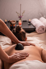 Woman in a spa receiving a relaxation massage with scented candles, incense, scent flowers, and obsidian stones with towels. 3
