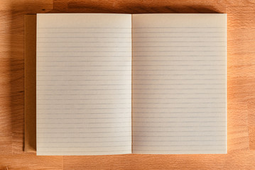 Open notebook or journal with blank pages on a bright wooden desk top, ready for copy or illustration
