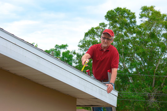 Wind mitigation inspection inspector on a ladder doing inspection on new roof to create a report and risk rating for homeowner to send to their insurance company to receive deductions in policy costs.