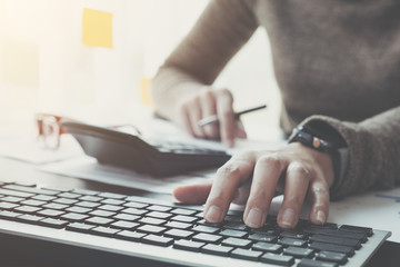 Close up of businessman or accountant hand holding pencil working on calculator to calculate financial data report, accountancy document and laptop computer at office, business concept