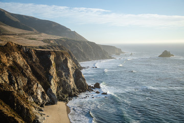 Fototapeta na wymiar Aerial drone view of the Big Sur coastline in California. Beautiful golden light hitting the side of the cliffs at sunset along the coastal road.