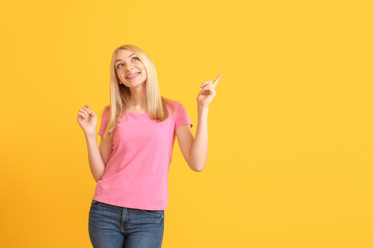 Young Woman With Dental Braces Showing Something On Color Background