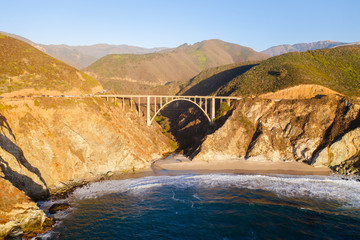 Big Creek Bridge in Big Sur, California. The photo is taken aerially from a drone as the sunsets in the distance, creating beautiful light on the bridge.