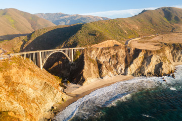Big Creek Bridge in Big Sur, California. The photo is taken aerially from a drone as the sunsets in the distance, creating beautiful light on the bridge.
