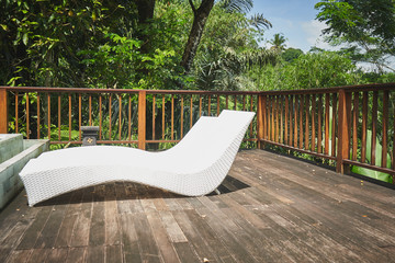 White deck-chair on the wooden hut near pool with tropic borest on background