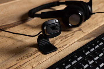 Home office theme: close up web cam, keyboard and headphones with microphone on wooden desk. concept of online work and video calls.