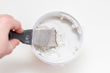 putty knife on worker hand and tub of white acrylic glazing putty