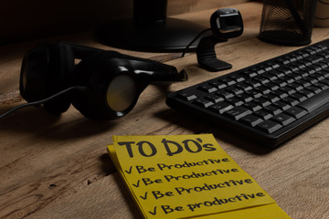 Home office theme: close-up.
To-do list to be productive with headband, microphone and computer on wooden desk. Productivity concept for online work. concept of avoiding distractions at home.
