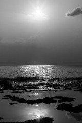A portrait black and white shot of the Indian Ocean and rocky beach of Neil island with sun and its reflection
